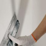 DIY Home Projects - Crop anonymous male worker in gloves holding putty knife while working at home