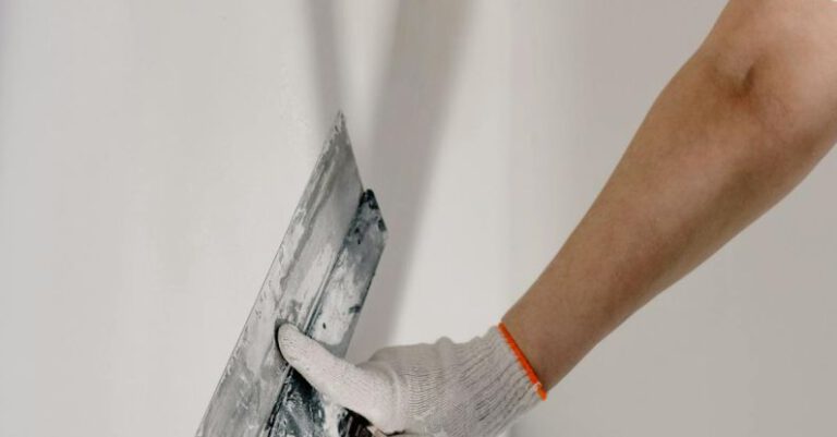 DIY Home Projects - Crop anonymous male worker in gloves holding putty knife while working at home