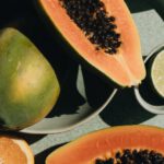 Vegetarian Diet - Top view of halves of ripe papaya together with oranges and limes placed on green round dishes and green fabric on white background
